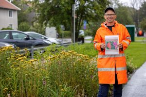 En man i orange regnrock står bredvid en plantering.
