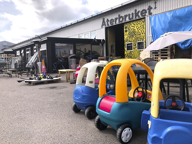 Bilden föreställer utemiljö utanför Återbruket på en av kommunens återvinningscentraler. Utanför står bland annat tre plastbilar.