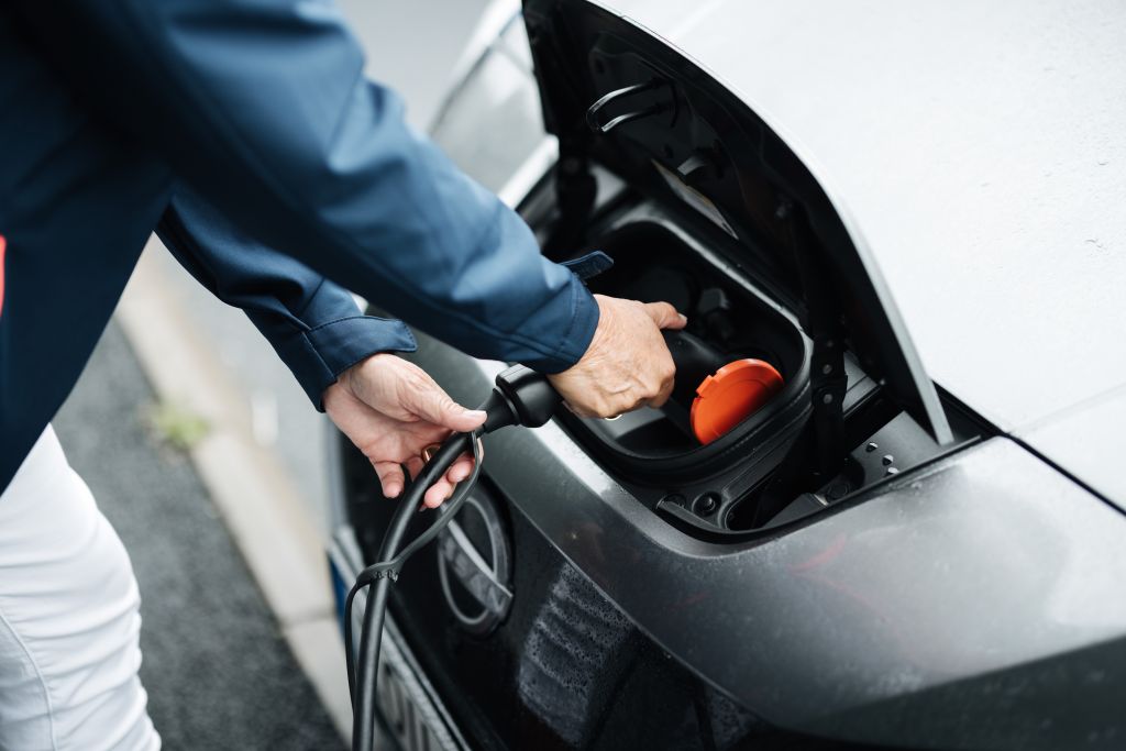 Foto på två händer som håller i en laddkabel och laddar en bil i motorhuven. 