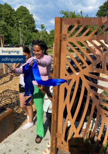 En glad kvinna klipper det blå invigningsbandet vid ingången till odlingsområdet.