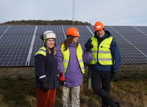 Tre personer i hjälm står vid solpaneler.