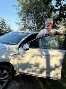 En man står vid en bil och ler in i kameran.