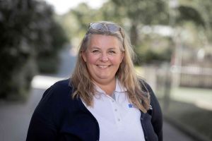 En kvinna i arbetskläder tittar in i kameran och ler.