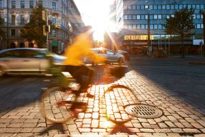 En människa cyklar förbi med stadsbild i bakgrunden.