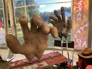 I ett tält sitter två jättestora dockhänder fast i arbetsbänkar. Bredvid ligger en sommarhatt.