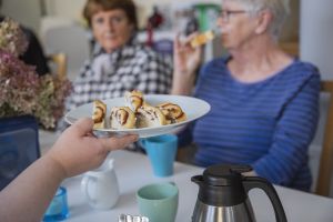 Ett foto av personer runt ett kaffebord som bjuds på vetebullar från ett fat.