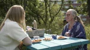 Två kvinnor fikar utomhus och pratar med varandra.