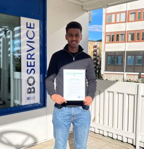 Nasir håller i sitt diplom utanför Boservice. 