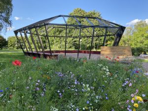 Träställning formad som en juvel. En träbänk och liten rabatt med blommor framför.