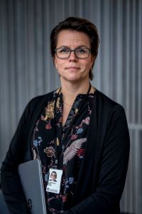 En kvinna med en dator i famnen tittar in i kameran.