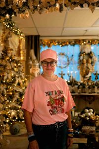 En kvinna med jultröja tittar in i kameran och ler. I bakgrunden julsaker.