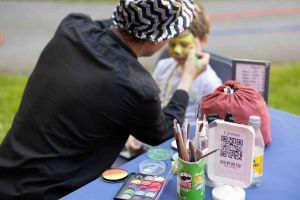 Man ser ryggen på en kvinna som målar ansiktet på ett barn.