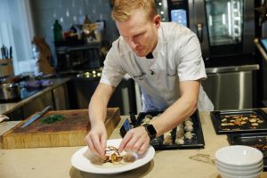 En man i kockkläder lägger upp mat på en tallrik.