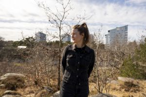 En ung kvinna blickar mot horisonten med hyreshus i bakgrunden.