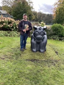 En glad man med blommor bredvid en skulptur föreställande en tjur.