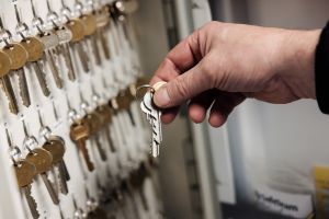 En hand håller i ett par nycklar. Fler nycklar hänger i bakgrunden.
