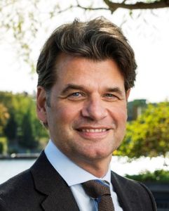 En man i kostym och slips tittar in i kameran och ler.