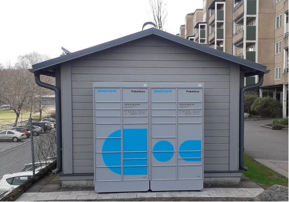 Postnords paketbox placerad mot en husvägg. 