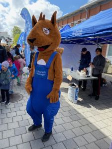 Reture, som är Bostadsbolagets maskot, är med på Tuvedagen. I bakgrunden står två av Bostadsbolagets medarbetare i ett blått tält.