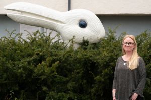 En kvinna tittar in i kameran bredvid ett konstverk.