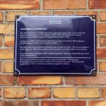 En plåtskylt på en husfasad som berättar mer om husets historia.