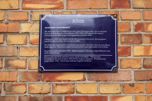 En plåtskylt på en husfasad som berättar mer om husets historia.