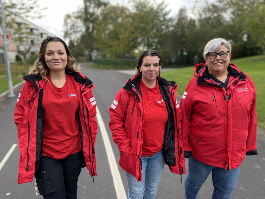 De tre trygghetsvärdarna promenerar på en väg iklädda röda jackor.