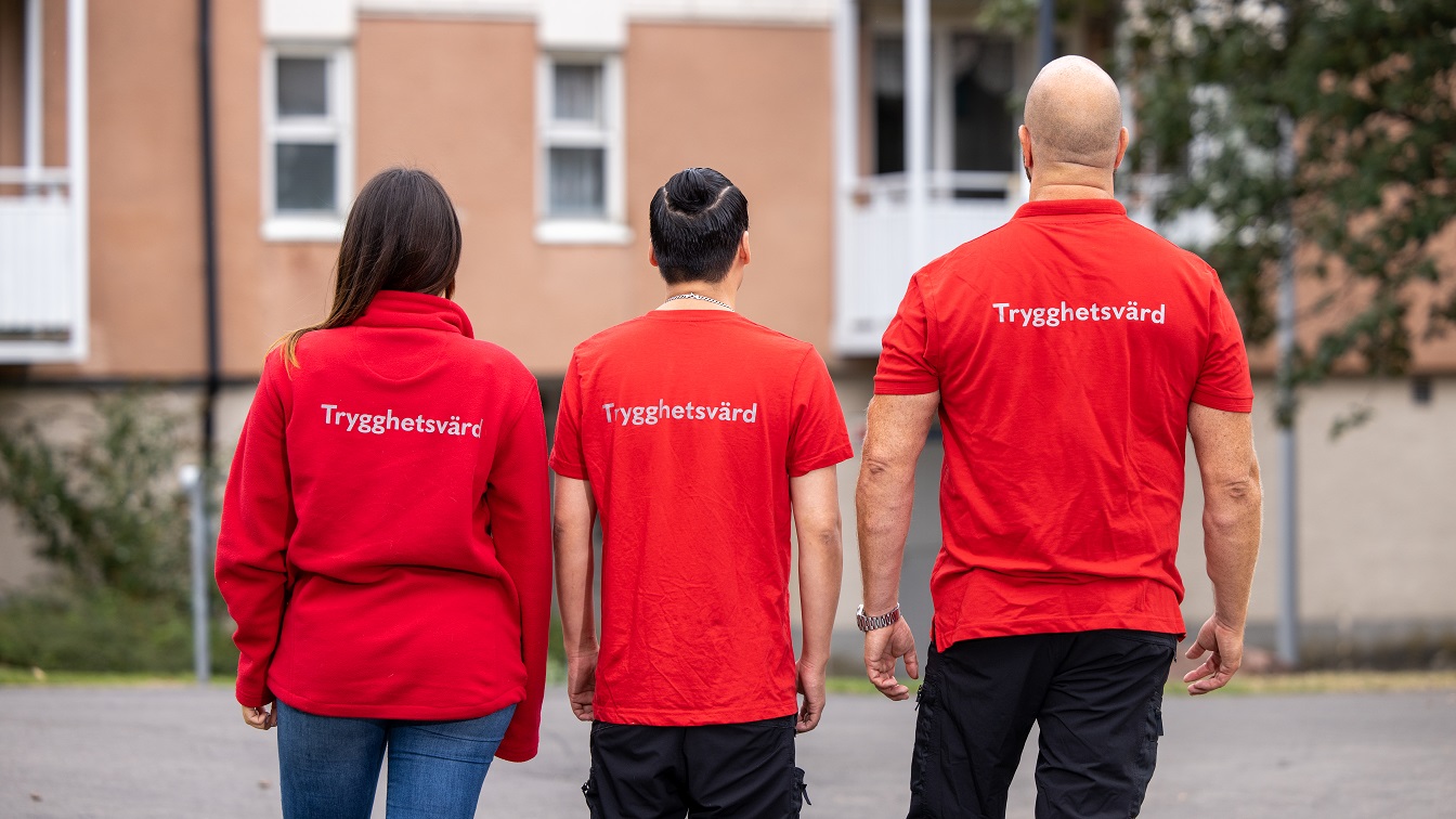 Tre trygghetsvärdar i röda tröjor står bredvid varandra med ryggen mot kameran.