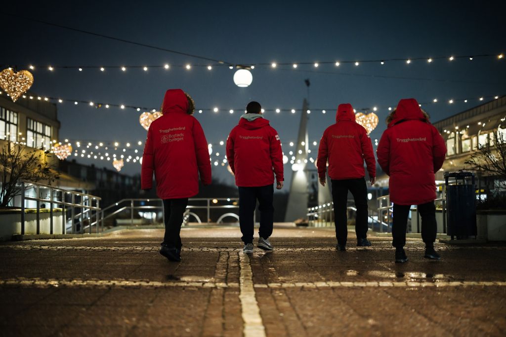 Man ser ryggen på fyra Trygghetsvärdar i röda vinterjackor. De går bort från bild.