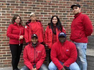 Gruppbild på sex trygghetsvärdar i röda jackor. Tre kvinnor och tre män. Alla män bär keps.