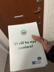 Foto på en flyer som vi delade ut i brevlådor med texten vi vill ha nya poolare. En fastighetsvärd håller en bunt i handen utanför en lägenhetsdörr. 