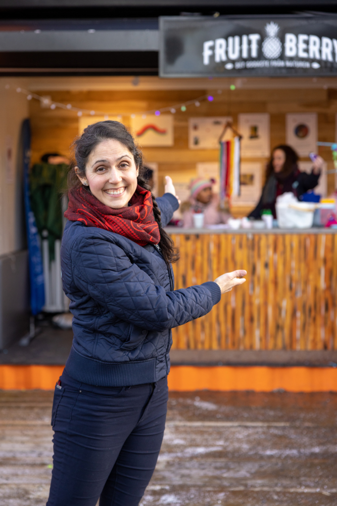 En kvinna ler mot kameran och visar bortåt med armarna.