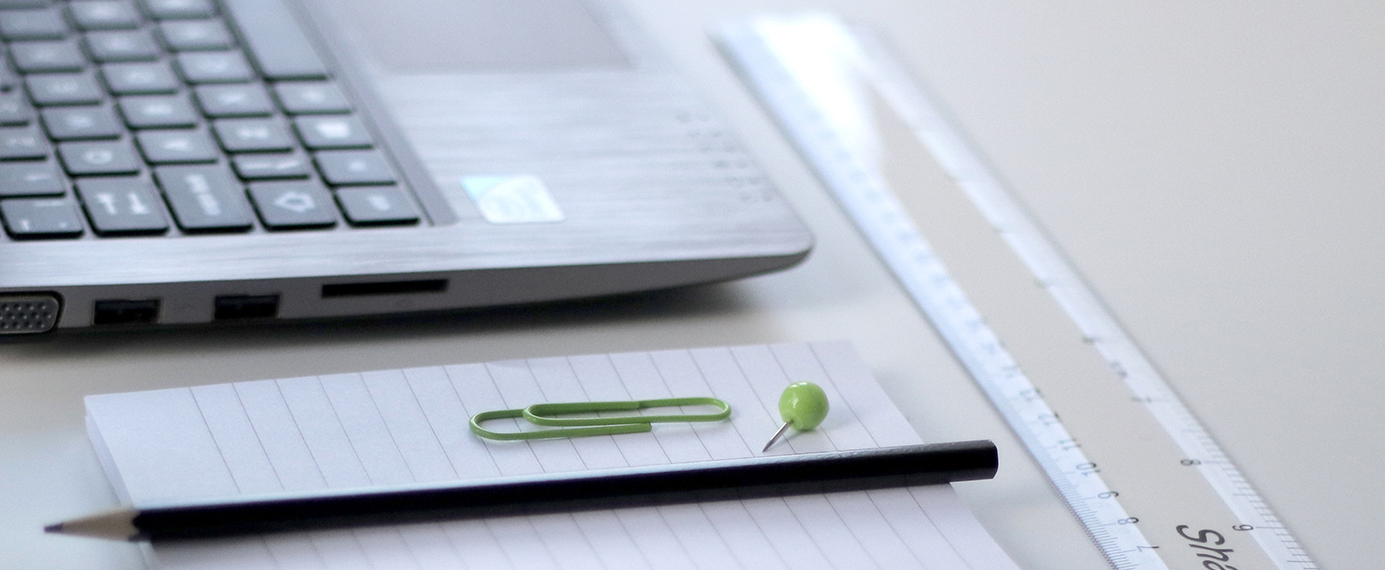 Bilden visar en dator, anteckningsblock och en penna