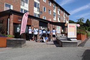 Designklubbens handledare står med ryggen mot kameran. På ryggen står Röhsskas "ö" i stort format. De står framför Orkanen som är lokalen där de brukar vara.