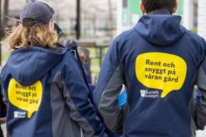 Två anställda vänder ryggen mot kameran och på ryggen står det Rent och snyggt på våran gård.