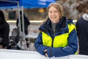 En kvinna i arbetskläder ler in i kameran.