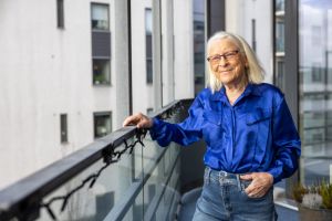 En kvinna står på sin balkong och ler mot kameran.